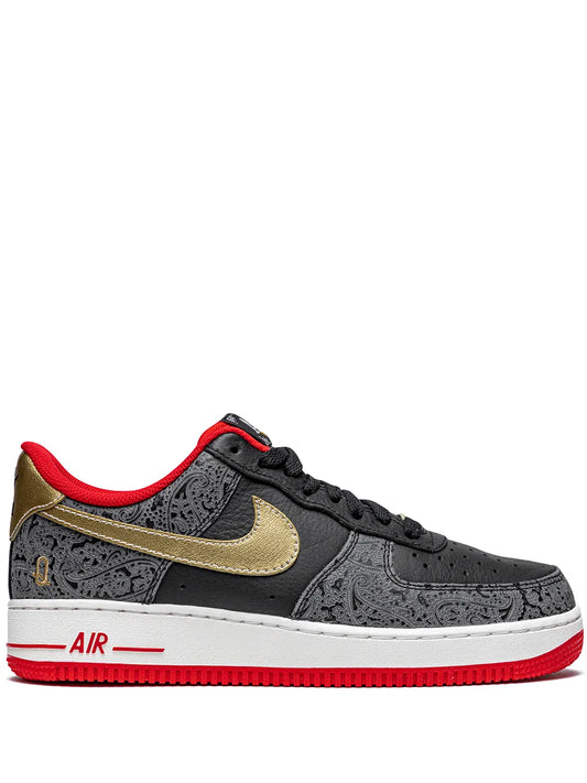 Black low-top sneakers with gold swoosh, red liner, and white midsole