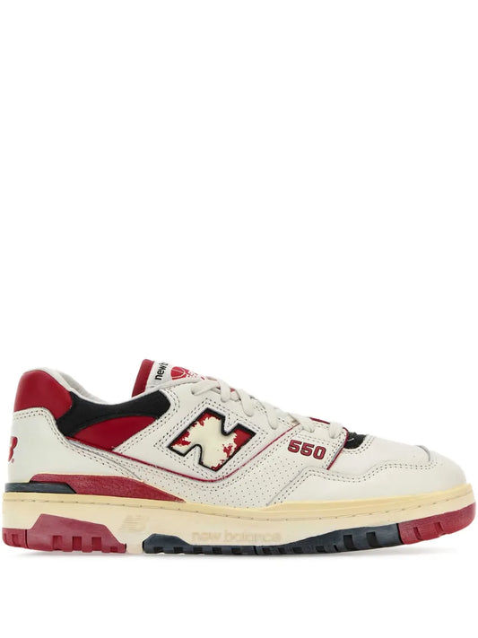 New Balance 550 sneakers in white, red, and black; lace-up with side N logo.