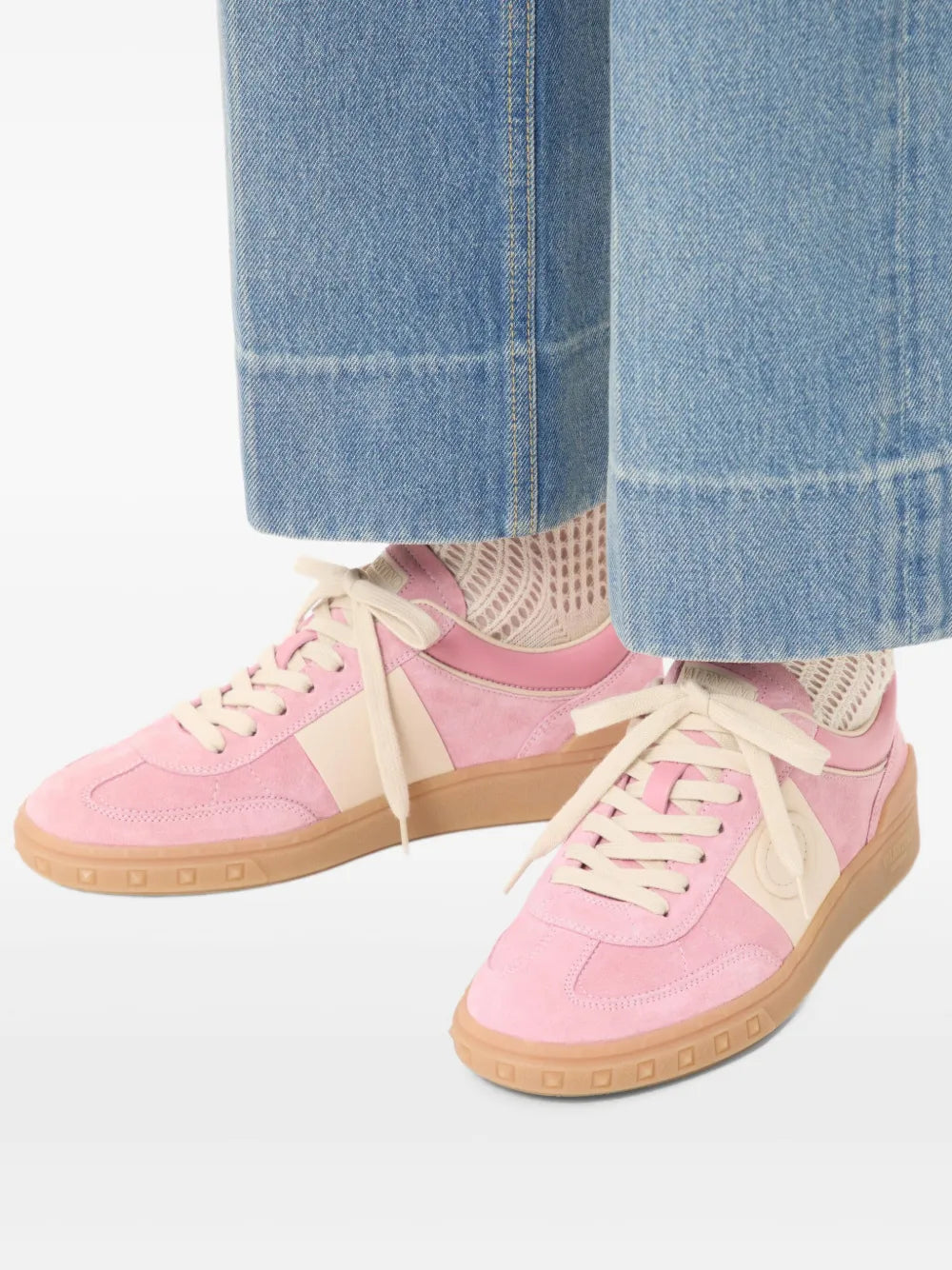 Pink sneakers worn with blue jeans; lace-up design and tan rubber sole