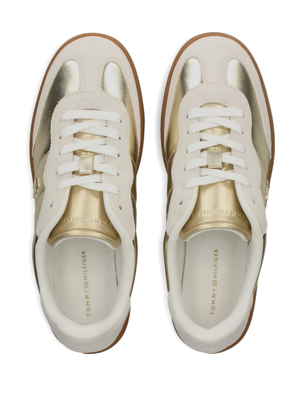 White low-top sneakers, toe and laces visible with gold logo detail