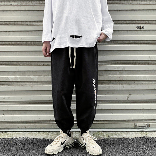 Black jogger trousers with drawstring waist, ribbed cuffs, and vertical white script logo