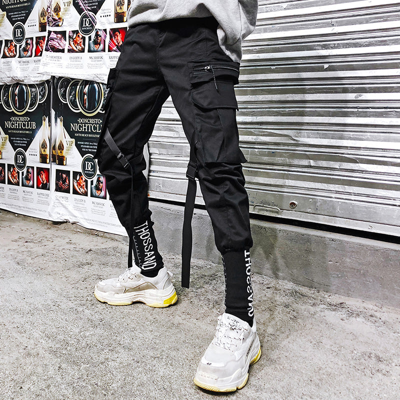 Black cargo pants with flap cargo pockets and straight fit, side tie detail.