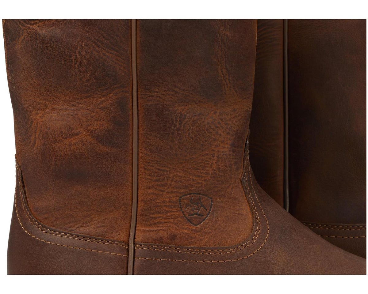 Men's distressed brown roper boot close-up, leather texture with stitched panel and emblem.